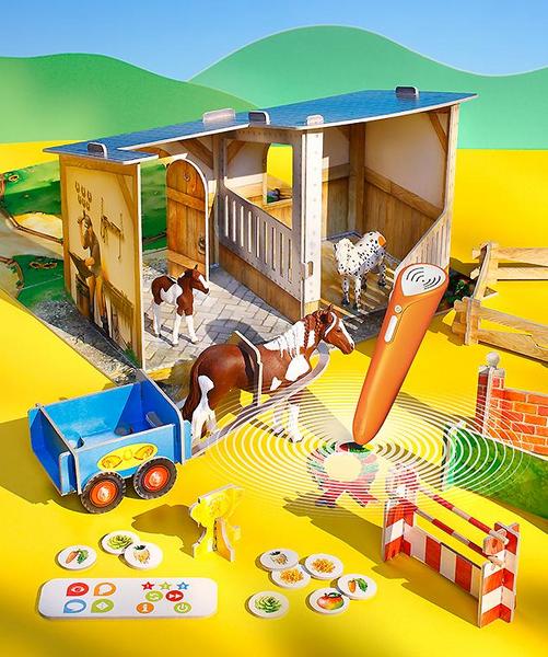 Ein Spielzeugset mit einem Holzstall, Pferden, einem blauen Wagen und verschiedenen Spielkarten. Ein orangefarbener Mikrofon ähnlicher Gegenstand sendet Schallwellen aus. Der Hintergrund zeigt grüne Hügel unter einem blauen Himmel.