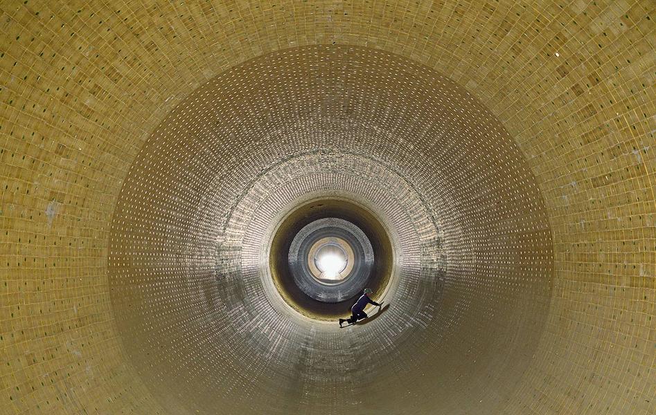 Drehofenausmauerung Eine perspektivische Ansicht des Innenraums eines großen, zylindrischen Behälters aus Steinen oder Platten. In der Mitte ist eine Lichtquelle sichtbar, während eine Person am Boden arbeitet. Die Wände sind rhythmisch strukturiert und reflektieren das künstliche Licht.