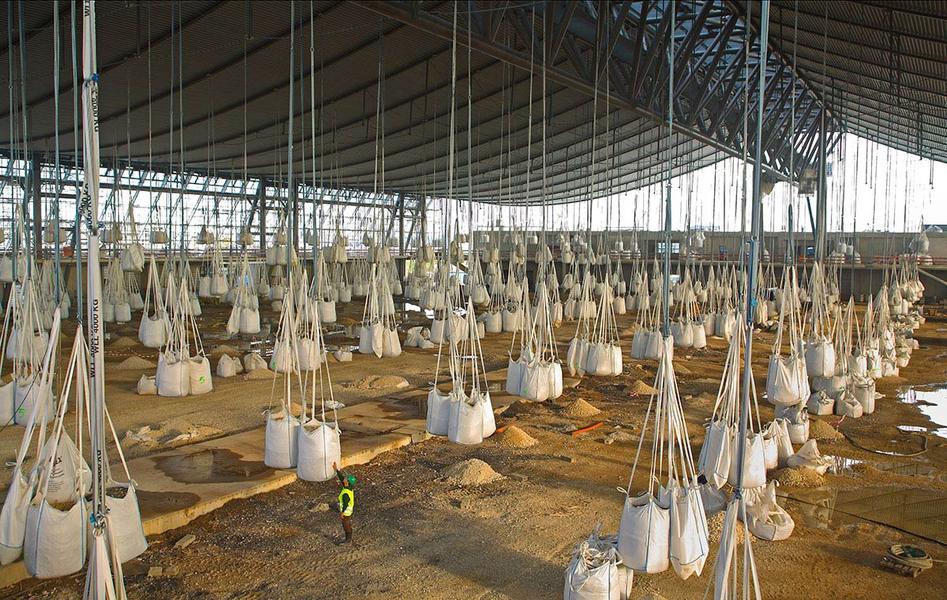 Baustelle Landesmesse Stuttgart Ein großer Lagerraum mit vielen hängenden Säcken, die mit Material gefüllt sind. Ein Arbeiter in gelber Sicherheitskleidung steht am Boden zwischen den Säcken. Die Wände des Raumes sind aus Metall und der Boden ist uneben.