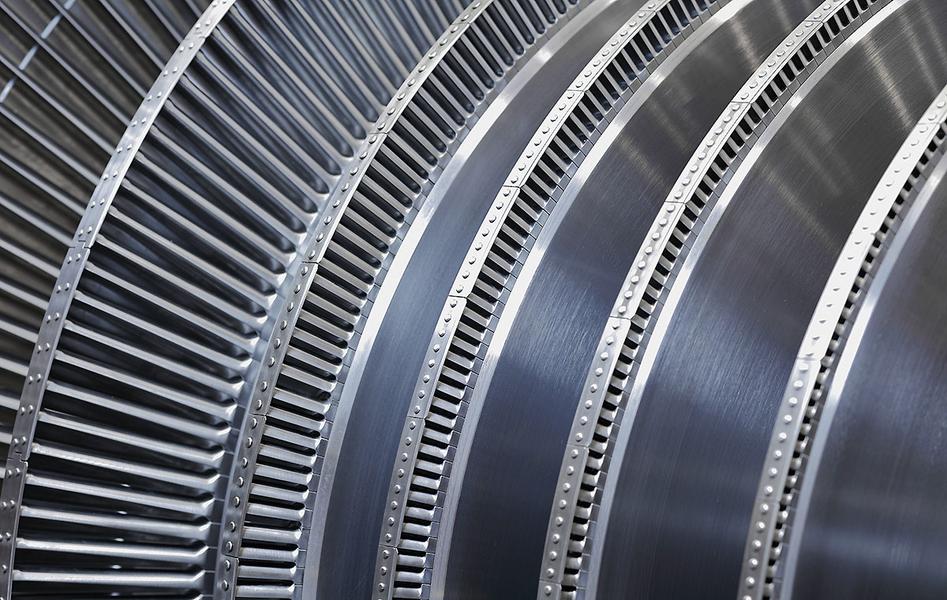 Dampfturbine Nahaufnahme von mehreren metallenen Turbinenschaufeln, die spiralförmig angeordnet sind. Die Oberfläche ist glänzend und zeigt feine Rillen sowie präzise Befestigungsdetails. Die Struktur deutet auf eine komplexe technische Konstruktion hin.
