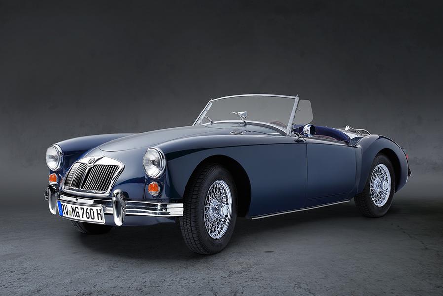 MGA 1600 Roadster Front Ein blauer Oldtimer-Cabriolet mit offenem Verdeck steht auf einer neutralen, grauen Fläche. Die glänzenden Felgen und der Charme des klassischen Designs heben sich von der dunklen Hintergrundfarbe ab.