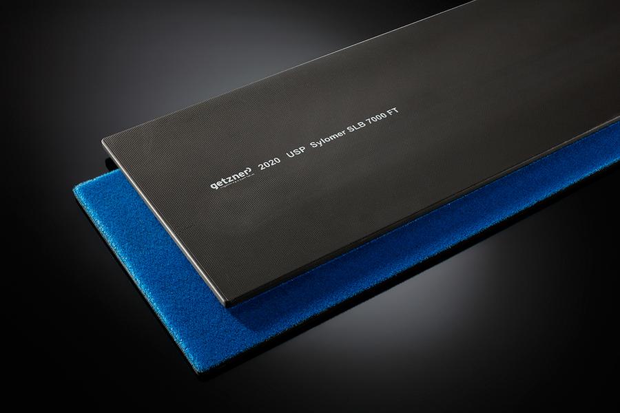 SL-NG Eine Metallplatte in Schwarz mit eingravierten Zahlen und Begriffen, die auf einem blauen Schaumstoffuntergrund liegt. Die Platte ist flach und länglich, der Hintergrund ist dunkel und hebt die Objekte hervor.