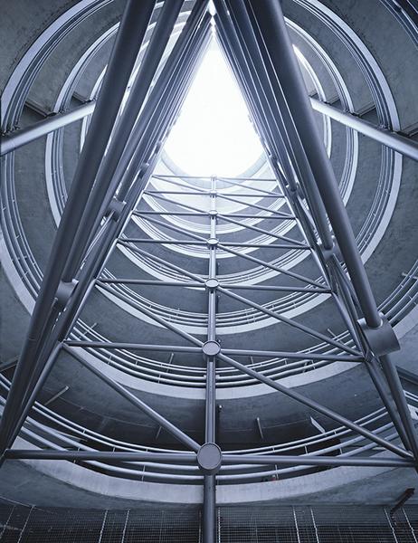 Parkhaus Ulm Ein Blick nach oben in einen modernen, zylindrischen Raum mit sichtbaren Stahlträgern. Das Licht strömt von oben durch eine kreisförmige Öffnung, während die Wände aus Beton und Stahl konstruiert sind. Die Struktur vermittelt ein Gefühl von Höhe und Raum.