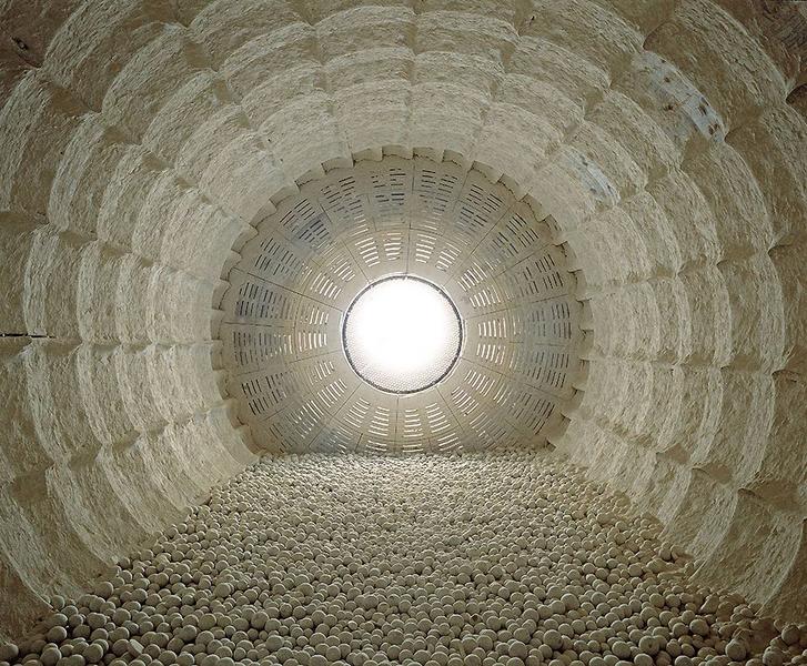 Innenansicht einer Rohmuehle Eine Ansicht von innen in einen großen, runden Behälter, der mit vielen weißen Kugeln auf dem Boden gefüllt ist. Am oberen Ende des Behälters ist ein helles Licht sichtbar, das den Eindruck von Tiefe und Weite vermittelt.