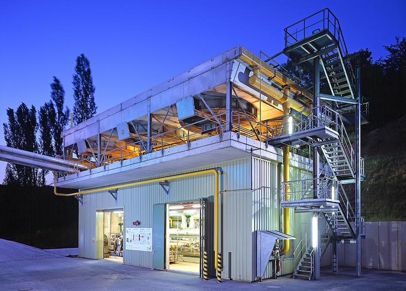 ORC Anlage in einem Zementwerk Eine moderne Industrieanlage bei Dämmerung, beleuchtet von gelbem und weißem Licht. Der Bau zeigt eine Stahlkonstruktion mit einer Treppe und mehreren Ebenen, umgeben von Bäumen im Hintergrund.