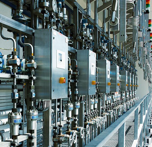 Abfuellanlage fuer technische Gase Nahaufnahme einer industriellen Anlagensteuerung mit mehreren silbernen Steuergeräten und Ventilen. Die Anordnung zeigt eine Reihe von Druck- und Temperaturmessgeräten sowie farbige Lichtanzeigen. Die Umgebung wirkt modern und technisch.