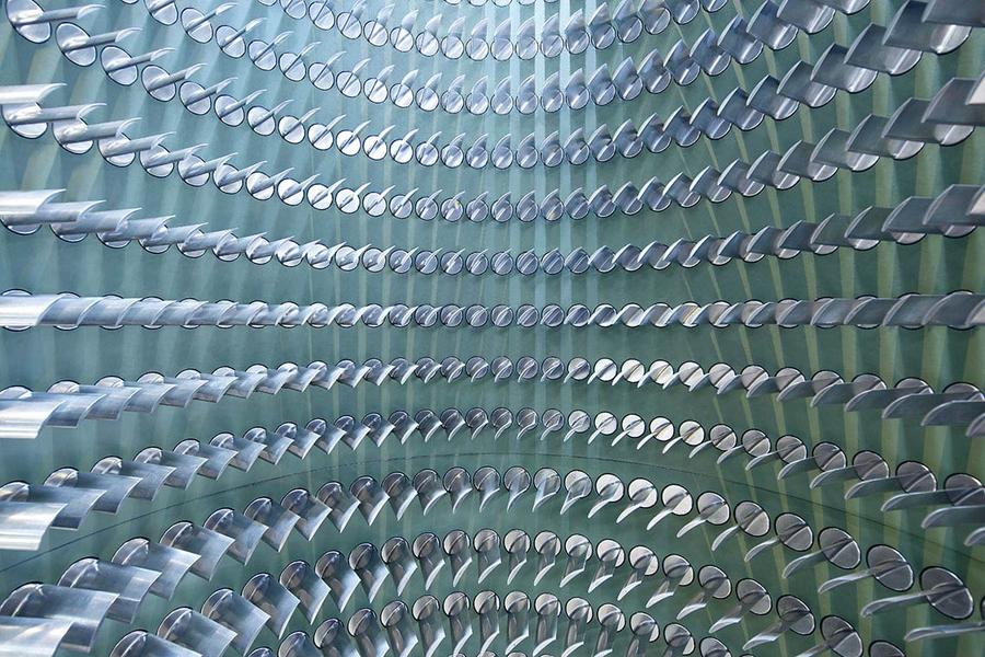 Schaufeltraeger Ein Muster von vielen silbernen Rohren, die kreisförmig angeordnet sind. Die Rohre sind teilweise spiegelnd und reflektieren das Licht, was einen dreidimensionalen Effekt erzeugt. Der Hintergrund ist in einem sanften Grünton gehalten.