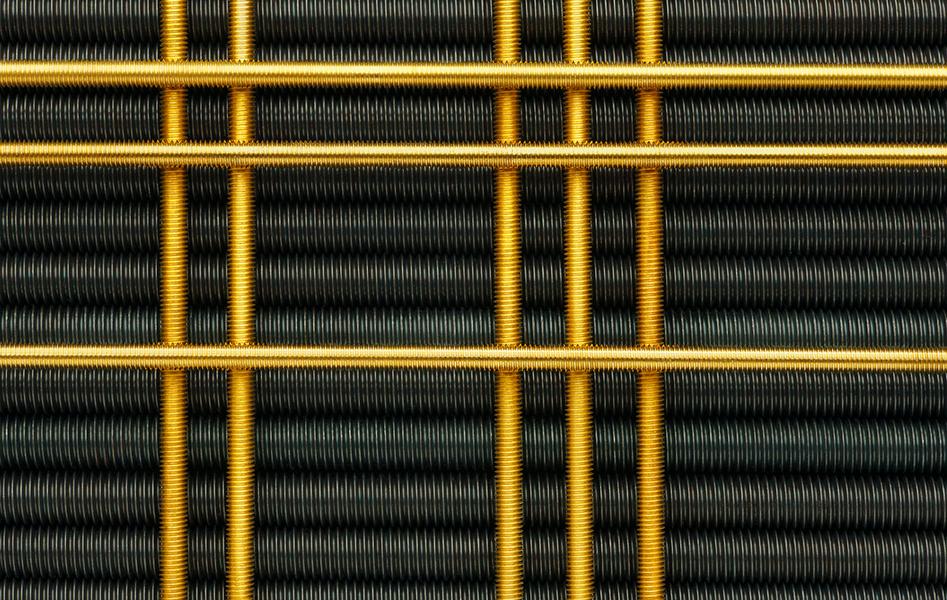 Gewindestangen Nahaufnahme von Drahtgeflecht in schwarzer und goldener Farbe, das ein grafisches Muster bildet. Die schwarzen Drahtschlingen sind in Reihen angeordnet, während die goldenen Drähte quer verlaufen und ein strukturiertes, industrielles Design erzeugen.