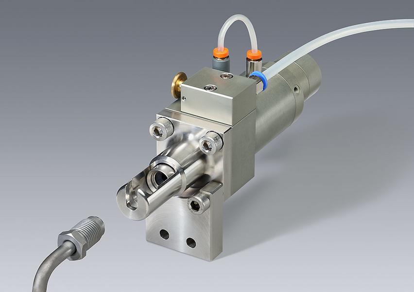 Eine präzise Maschinenteileinheit, bestehend aus einem metallischen Gehäuse mit Anschlüssen und Schläuchen. Der Fokus liegt auf dem Ventilmechanismus, der für industrielle Anwendungen eingesetzt wird. Im Hintergrund ist eine neutrale graue Fläche.