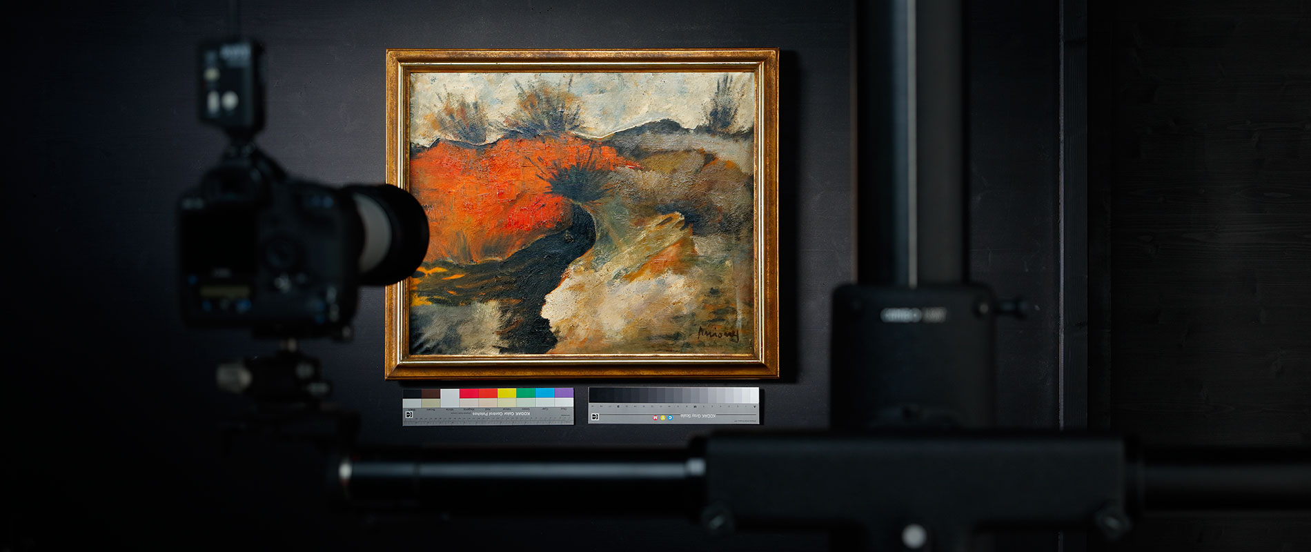 Reproduktion eines Gemälde Ein Gemälde mit kräftigen roten und grauen Farbtönen ist in einem Rahmen an einer Wand zu sehen. Im Vordergrund steht eine Kamera auf einem Stativ, die auf das Kunstwerk gerichtet ist. Daneben befinden sich Farbmuster und Informationen zur Darstellung.