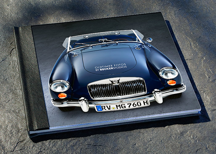 Fotobuch Studioaufnahme Ein graues Fotobuch liegt auf einer Oberfläche, das eine Abbildung eines klassischen blauen Autos zeigt. Auf dem Buchcover sind die Worte "Oldtimer Fotos by BEICKERSTUDIOS" zu sehen.