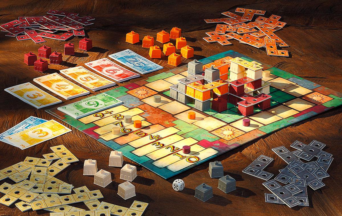 Ein Tisch mit einem aufgeräumten Brettspiel. In der Mitte liegt das Spielbrett mit bunten Spielfiguren und Karten. Rund um das Brett sind Stapel aus farbigen Spielsteinen und Geldscheinen verteilt. Ein Würfel liegt ebenfalls auf dem Tisch.