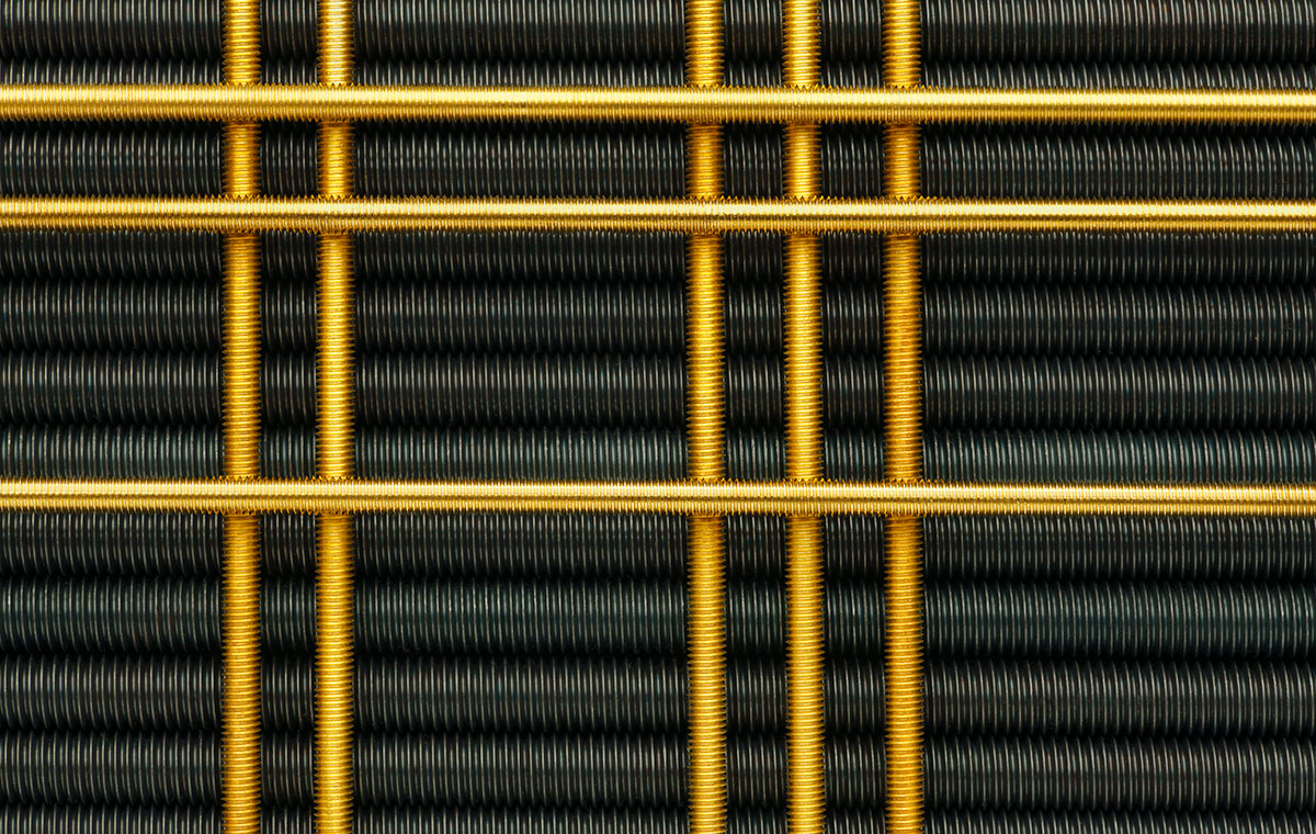 Gewindestangen Nahaufnahme von Drahtgeflecht in schwarzer und goldener Farbe, das ein grafisches Muster bildet. Die schwarzen Drahtschlingen sind in Reihen angeordnet, während die goldenen Drähte quer verlaufen und ein strukturiertes, industrielles Design erzeugen.