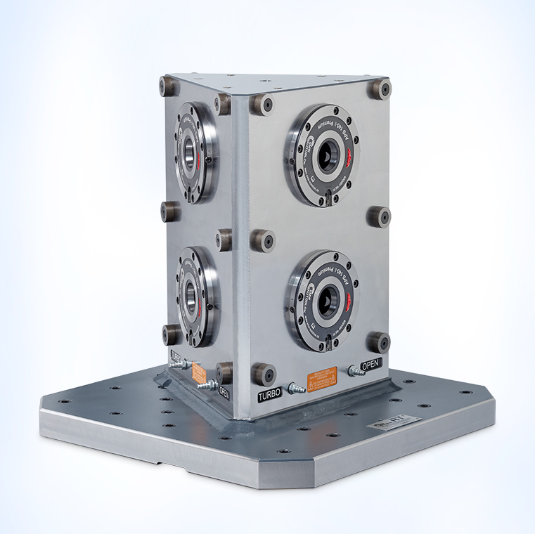 Ein quadratisches, metallisches Gerät mit vier runden Öffnungen auf den Seiten. Es steht auf einer flachen, rechteckigen Basis. Die Oberfläche ist glänzend und zeigt technische Details, einschließlich Beschriftungen wie "TURBO" und "OPEN".