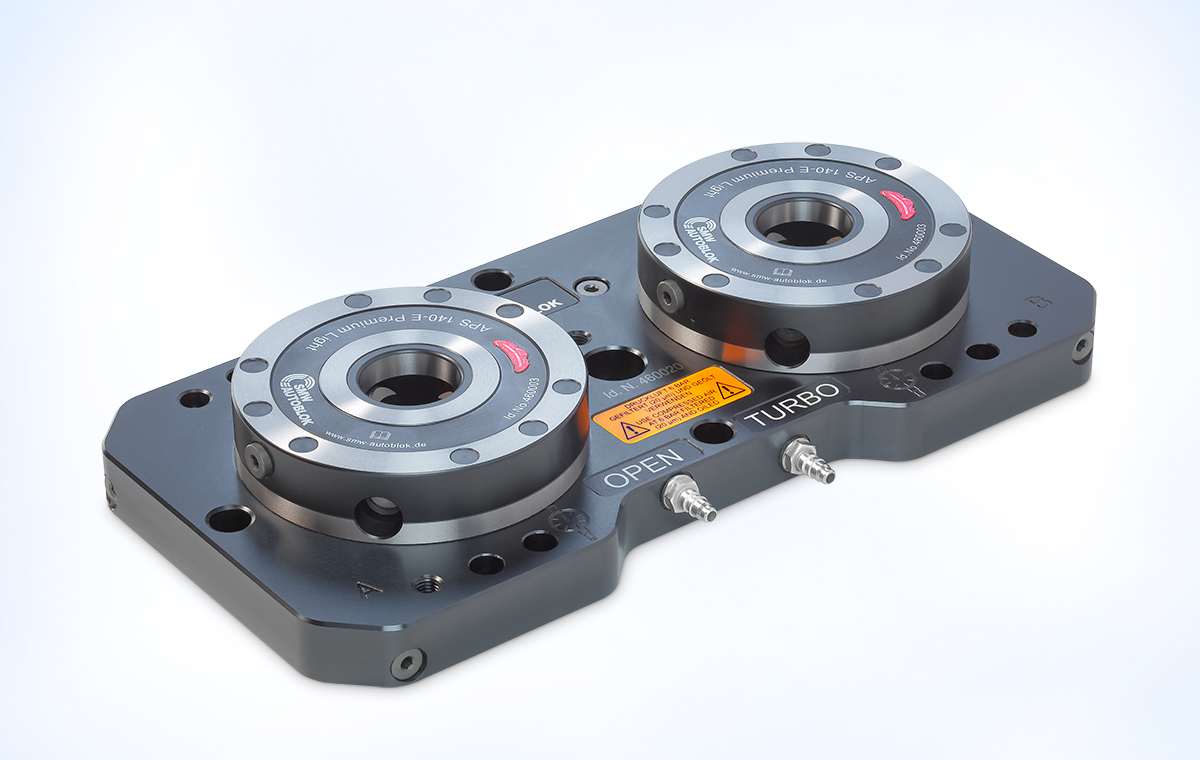 Schwarze Plattenkomponente mit zwei runden, metallischen Vorrichtungen auf der Oberseite. Jede Vorrichtung hat einen roten und silbernen Ring sowie Beschriftungen. Die Platte enthält zusätzliche Anschlüsse an der Seite, die auf technische Funktionen hinweisen.