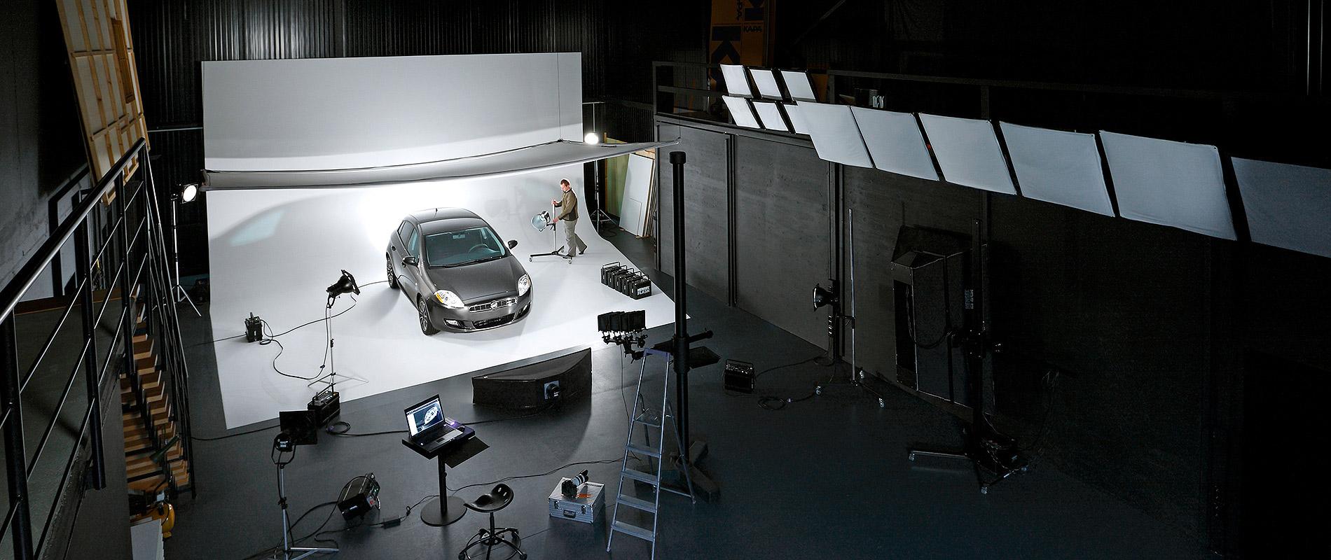 Firmengebaeude Becker Studios Ein Auto steht auf einem beleuchteten Fotostudio-Hintergrund. Rund um das Fahrzeug sind verschiedene Lichtquellen und Kamerastative angeordnet. Eine Person arbeitet im Hintergrund, um die Aufnahme vorzubereiten.