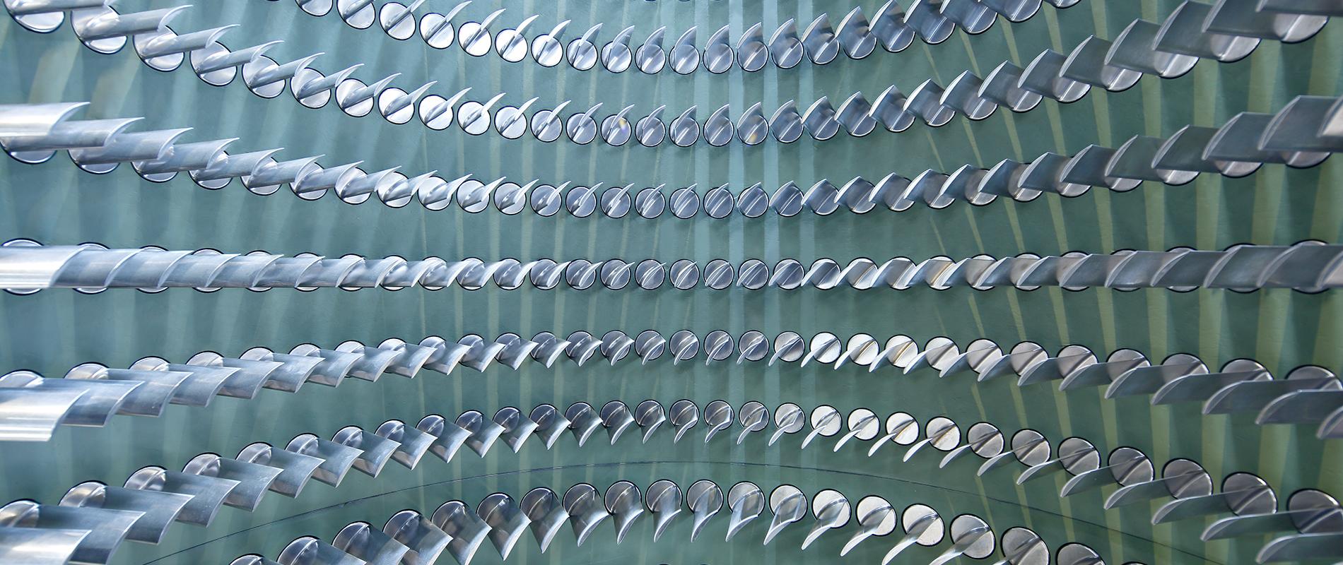 Eine visuelle Anordnung von vielen metallischen, gebogenen Objekten, die in einem spiralförmigen Muster angeordnet sind. Der Hintergrund ist in sanften Grüntönen gehalten, was das Gesamtbild harmonisch wirken lässt.