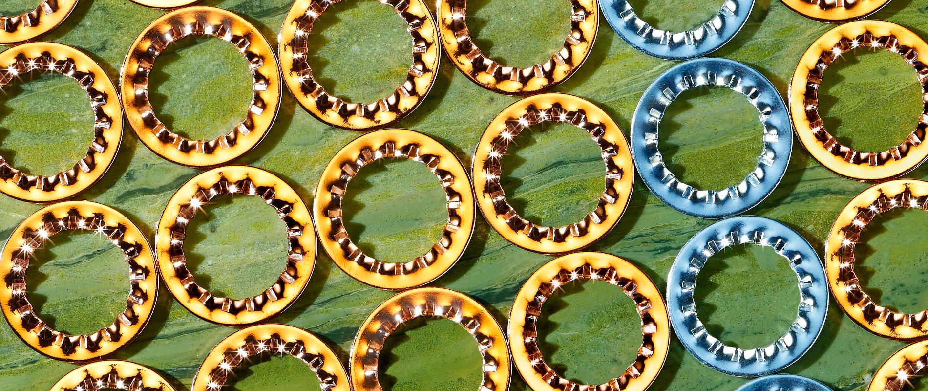 Eine Nahaufnahme von mehreren bunten Kronkorken in Gelb und Blau, die auf einer grünen Oberfläche angeordnet sind. Die Kappen haben gezackte Ränder und sind gleichmäßig verteilt.